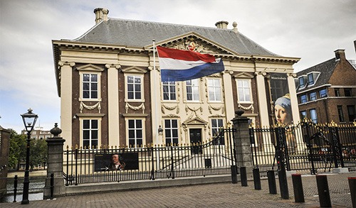 mauritshuis with red, white and blue flag of the netherlands and banner of vermeer's painting girl with the pearl earring
